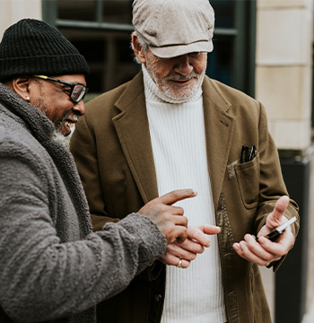Two older men with beards smile at something on a smartphone